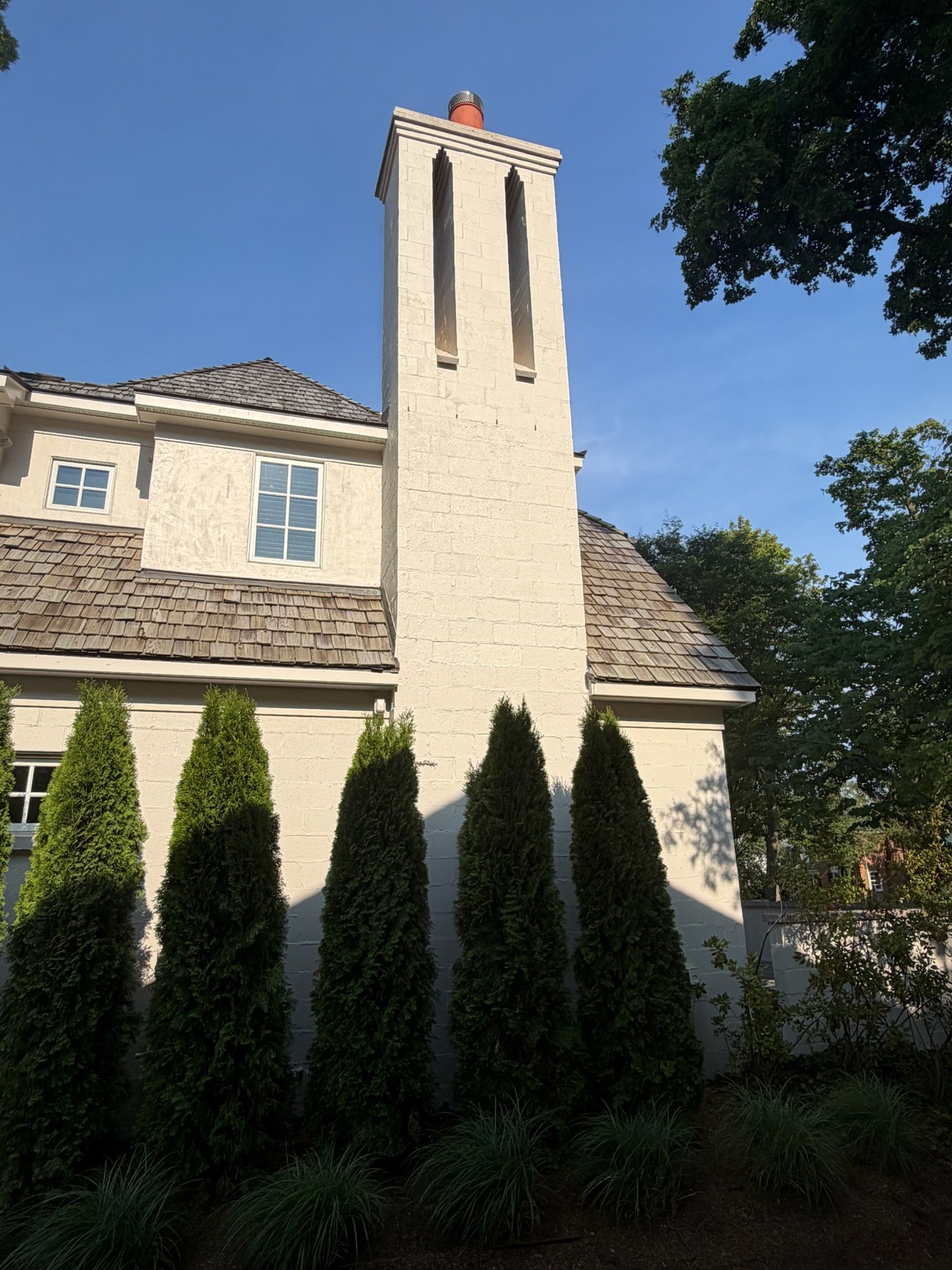Cream chimney on luxury home with arborvitae